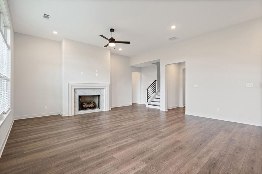 Spacious living area featuring wood-finish flooring, a fireplace with a white surround and marble-look tile, recessed lighting, and a ceiling fan Spacious living area featuring wood-finish flooring, a fireplace with a white surround and marble-look tile, recessed lighting, and a ceiling fan