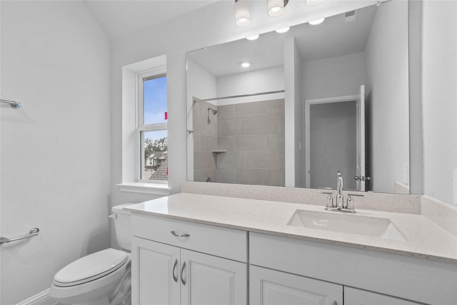 Secondary bathroom featuring an extended vanity cabinet with single bowl sink, chrome hardware, mirror, vanity lighting, tub/shower combination with tile surround, and tile flooring.