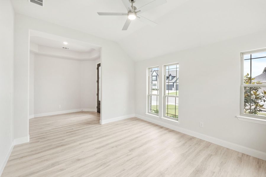 Empty bedroom with vaulted ceiling, ceiling fan, light wood floors, and two windows with neighborhood views
