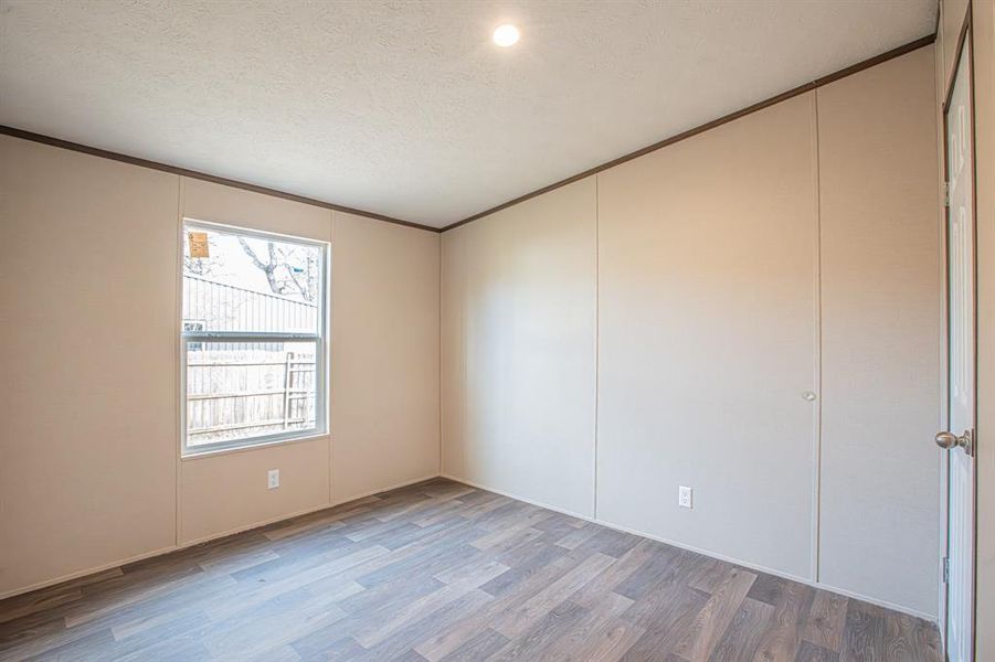 Unfurnished room with a textured ceiling, wood finished floors, and ornamental molding Unfurnished room with a textured ceiling, wood finished floors, and ornamental molding