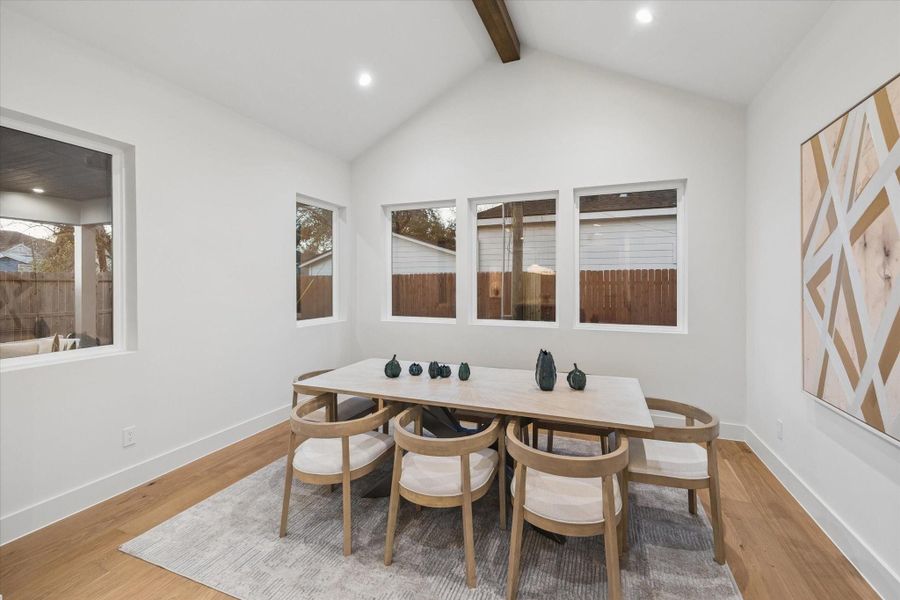 Elegant dining room featuring a soaring vaulted ceiling, exposed wood beam, and views of the backyard through large windows.