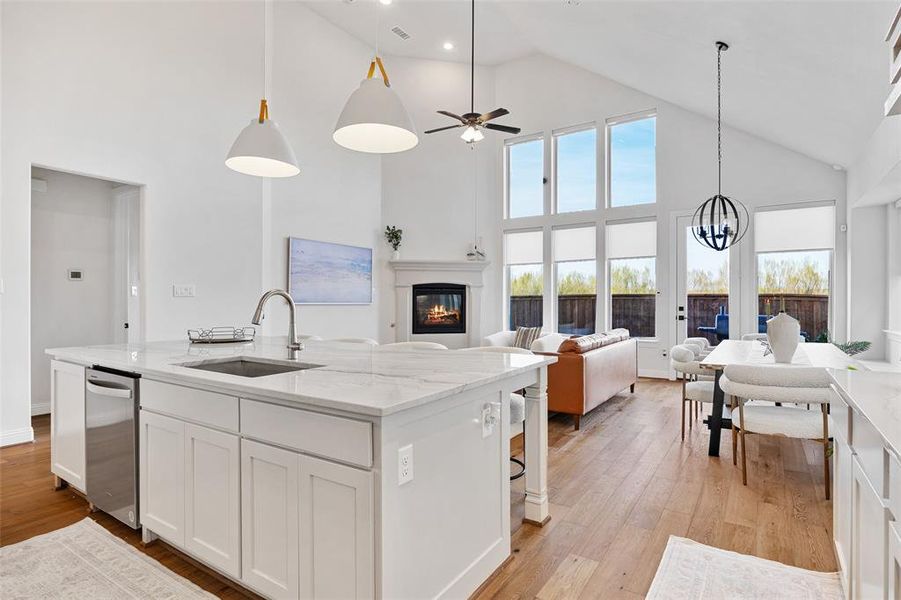 Kitchen with stainless steel dishwasher, a glass covered fireplace, open floor plan, high vaulted ceiling, and a sink