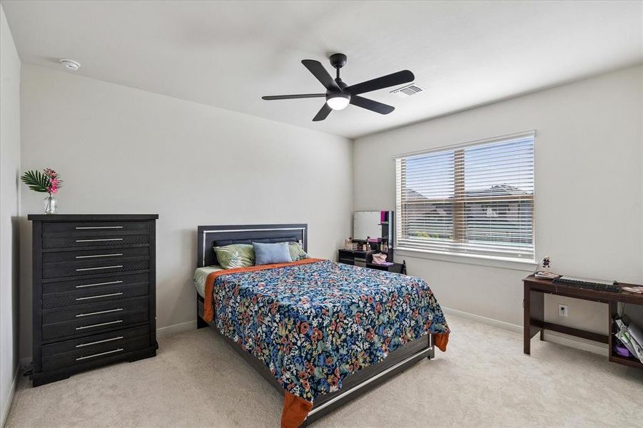 Carpeted bedroom featuring a large window with blinds, a ceiling fan with integrated lighting, and neutral wall tones Carpeted bedroom featuring a large window with blinds, a ceiling fan with integrated lighting, and neutral wall tones