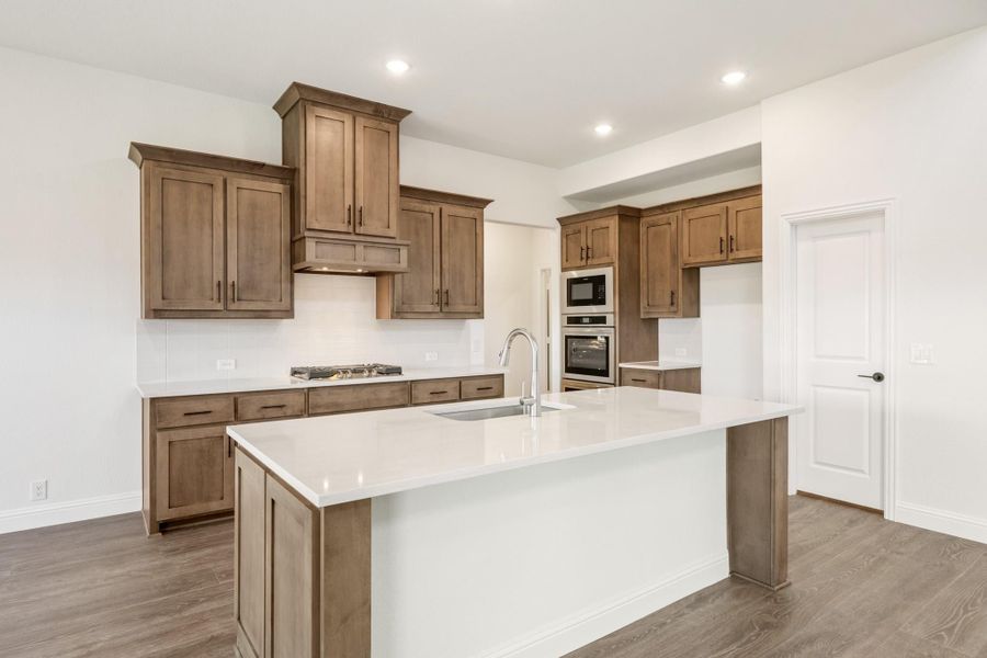 Kitchen with brown wood cabinets, large center island with sink, white countertops, and stainless steel double ovens