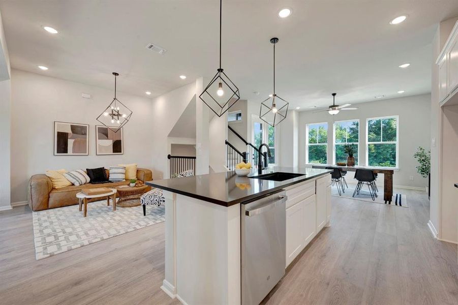 Open-concept living space featuring wood-finish flooring, recessed lighting, and a kitchen island with a dark countertop and integrated stainless steel dishwasher