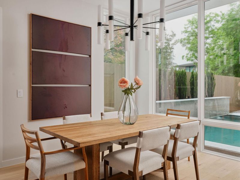 Dining area featuring wood-finish flooring, a contemporary chandelier, and large windows with exterior pool views