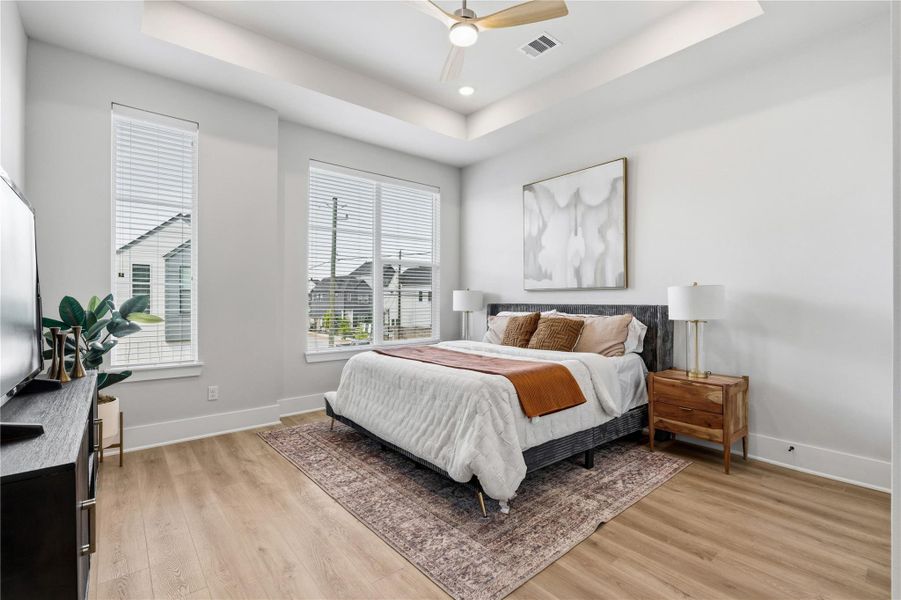 A spacious primary suite featuring tray ceilings and expansive windows that fill the room with natural light. A spacious primary suite featuring tray ceilings and expansive windows that fill the room with natural light.