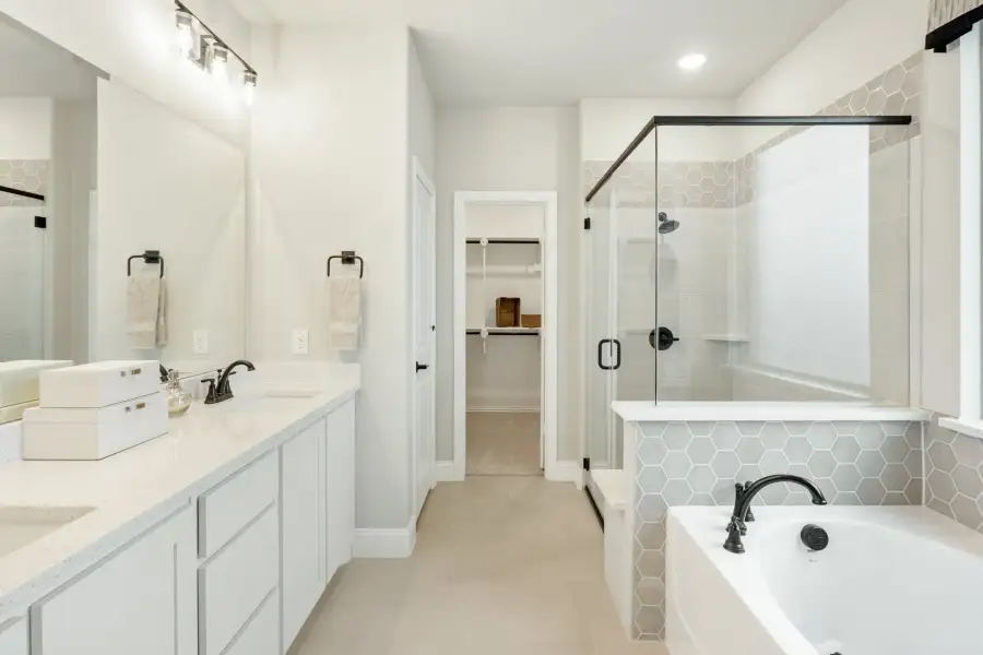Master bathroom with double vanity, soaking tub, glass shower, and walk-in closet entrance
