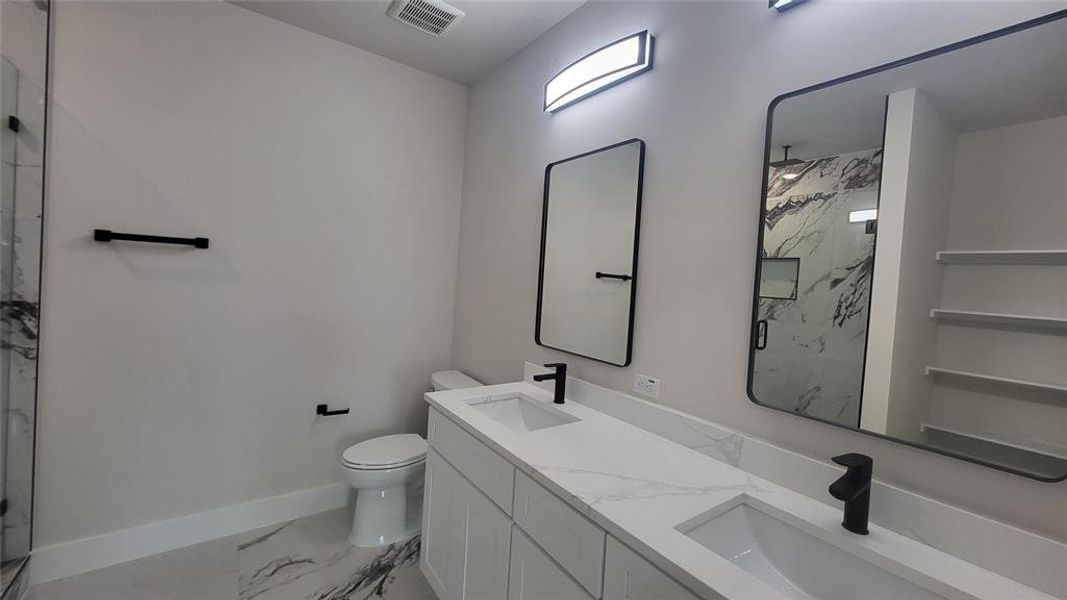 Full bath featuring visible vents, toilet, a marble finish shower, and a sink