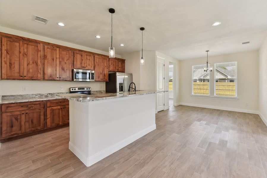 Kitchen featuring visible vents, light wood-style flooring, stainless steel appliances, brown cabinetry, and hanging light fixtures