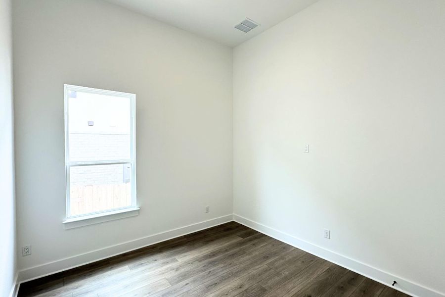 A well-lit room showcases rich hardwood flooring and a single window.