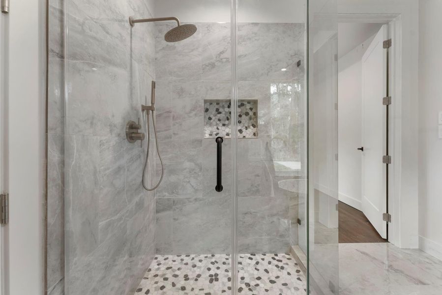 This photo showcases a modern, elegant shower with glass doors, tile walls, and a pebble stone floor. It features a rainfall showerhead and a built-in niche for storage, offering a luxurious and functional bathroom experience.