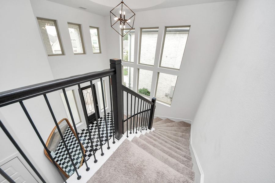 A bright, modern entryway with a staircase featuring black railings leads to a landing with large windows. The floor below is checkered, creating a stylish and welcoming atmosphere. A bright, modern entryway with a staircase featuring black railings leads to a landing with large windows. The floor below is checkered, creating a stylish and welcoming atmosphere.