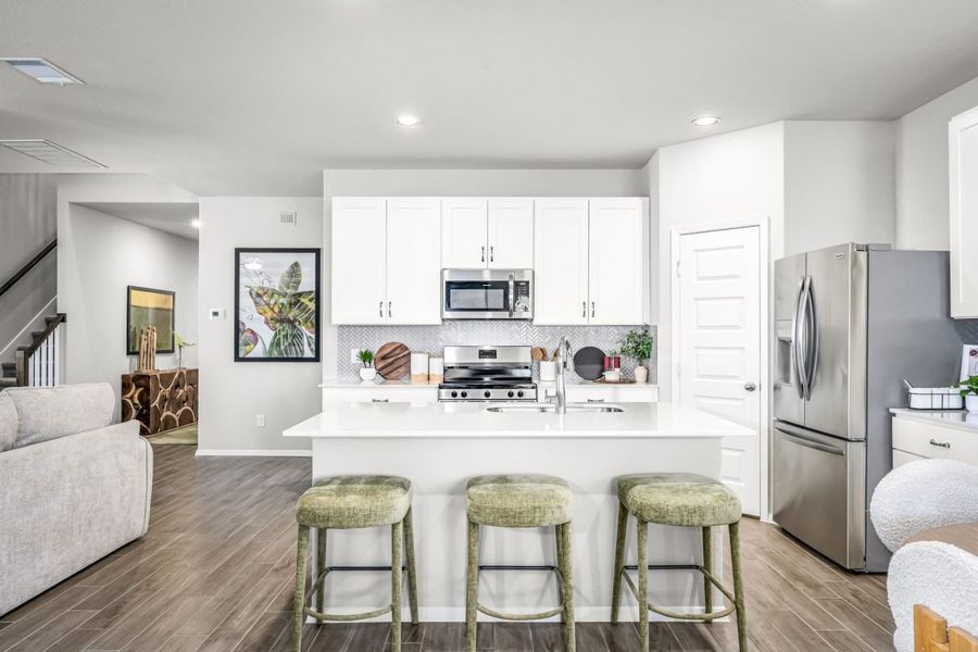 Image of kitchen with white cabinets with white countertops, wood flooring, and a white painted wall.
