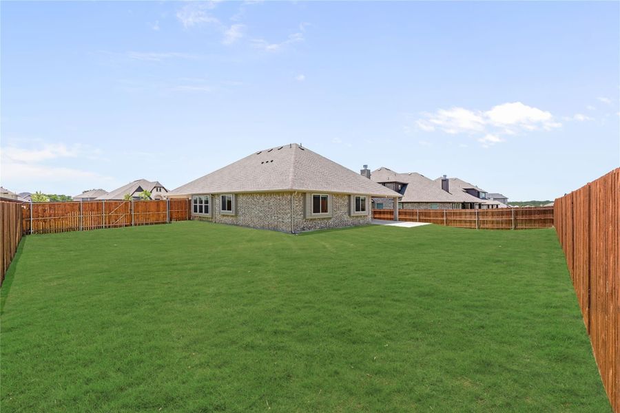 Brick home rear view with large grassy backyard enclosed by wood privacy fence