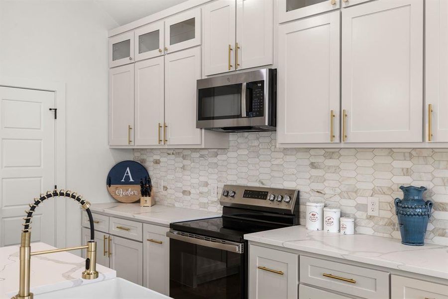 Kitchen featuring light stone countertops, appliances with stainless steel finishes, white cabinets, and backsplash