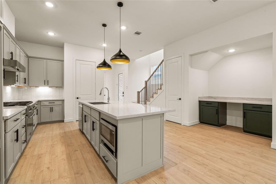 Functional design features — island microwave drawer inset, stainless steel appliance package, and custom built-in workstation nook tucked neatly under the staircase.
