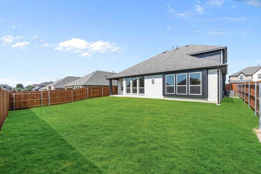 Backyard with large green lawn, wood privacy fence, and brick home with covered patio and large windows Backyard with large green lawn, wood privacy fence, and brick home with covered patio and large windows