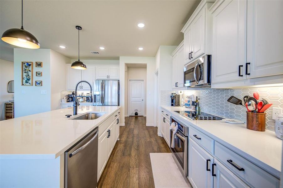 Kitchen with white cabinetry, stainless steel appliances, a center island with sink, and dark wood-style flooring