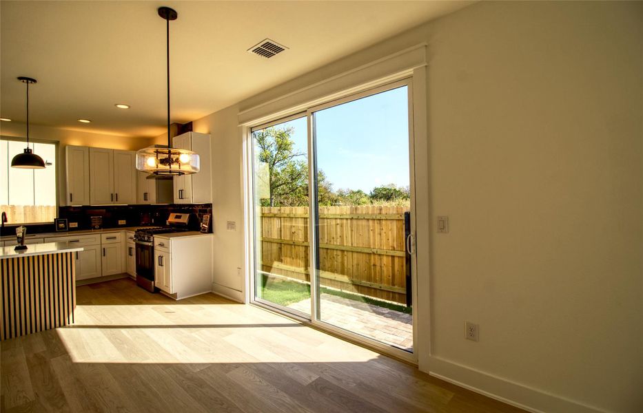 Kitchen featuring pendant lighting, gas range, tasteful backsplash, light wood-type flooring, and white cabinets
