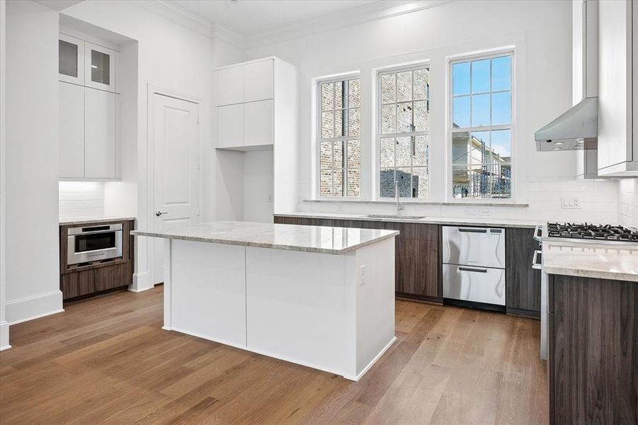 Kitchen featuring a central island with a light-toned countertop, wood-finish flooring, white upper cabinetry, dark wood-finish lower cabinetry, and a built-in microwave Kitchen featuring a central island with a light-toned countertop, wood-finish flooring, white upper cabinetry, dark wood-finish lower cabinetry, and a built-in microwave