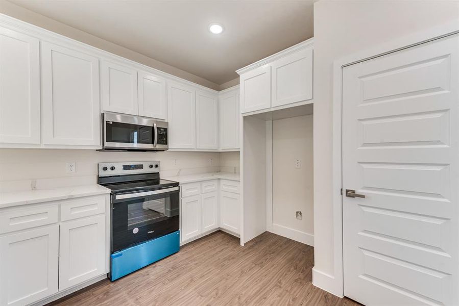 Kitchen featuring stainless steel appliances, light hardwood / wood-style floors, white cabinetry, and light stone counters