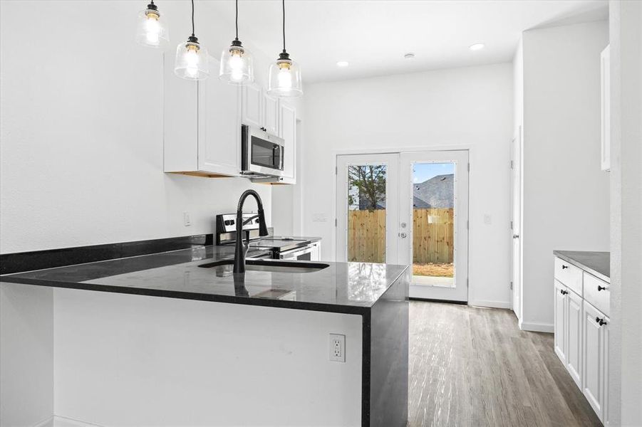 Kitchen with stainless steel appliances, hanging light fixtures, white cabinetry, and kitchen peninsula