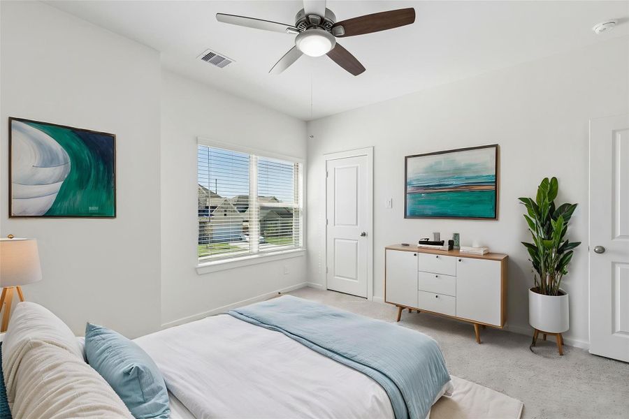 This upstairs bedroom features neutral carpeting, a ceiling fan, and large windows with integrated blinds. The space has been virtually staged to show its potential as a guest retreat.