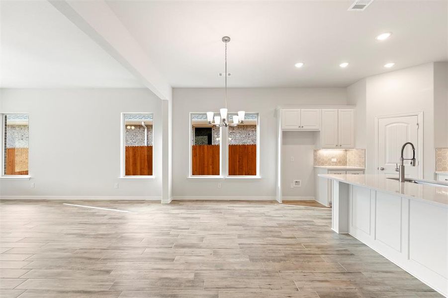 Kitchen with white cabinetry, tasteful backsplash, a chandelier, hanging light fixtures, and light stone counters