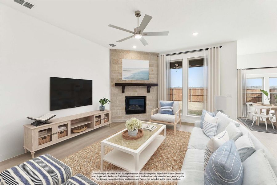 Living room with stone corner fireplace, ceiling fan, wall-mounted TV, and large windows with backyard view Living room with stone corner fireplace, ceiling fan, wall-mounted TV, and large windows with backyard view