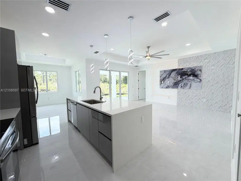 Open-concept kitchen featuring an oversized island with quartz countertops, custom cabinetry, recessed lighting, stone-finish wall cladding, and oversized light-colored floor tiles