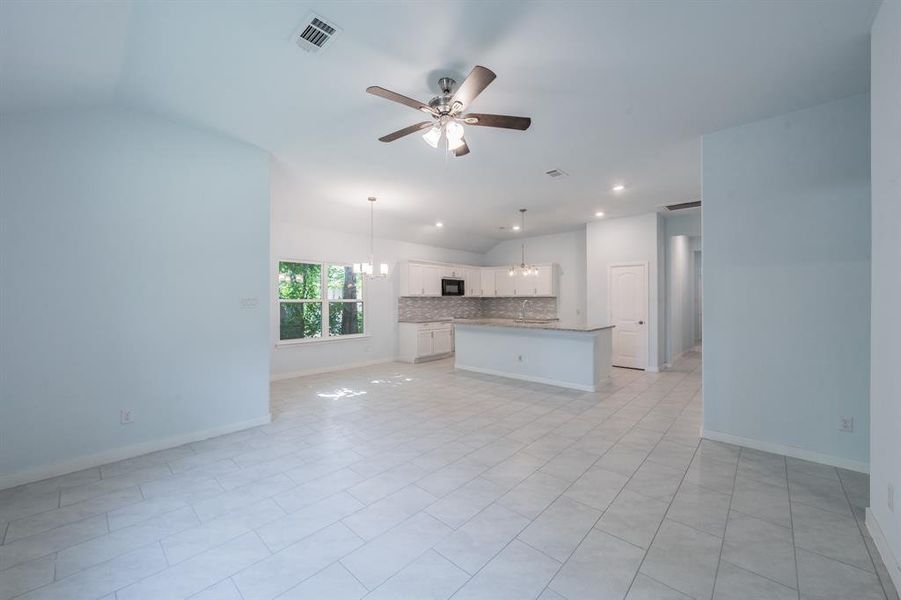 Unfurnished living room with a ceiling fan, lofted ceiling, recessed lighting, a chandelier, and light tile patterned floors Unfurnished living room with a ceiling fan, lofted ceiling, recessed lighting, a chandelier, and light tile patterned floors