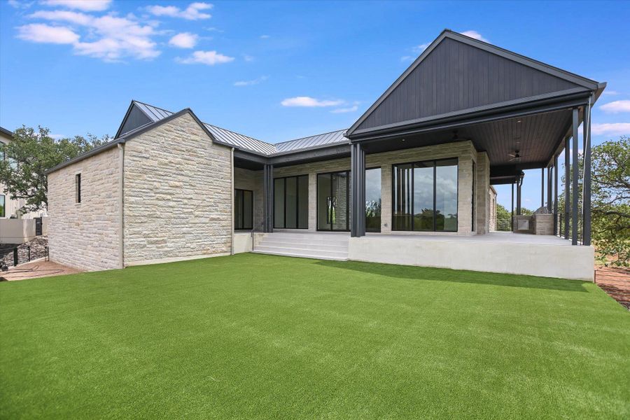 A modern stone and dark wood home with a spacious covered patio and verdant lawn awaits outdoor enjoyment.