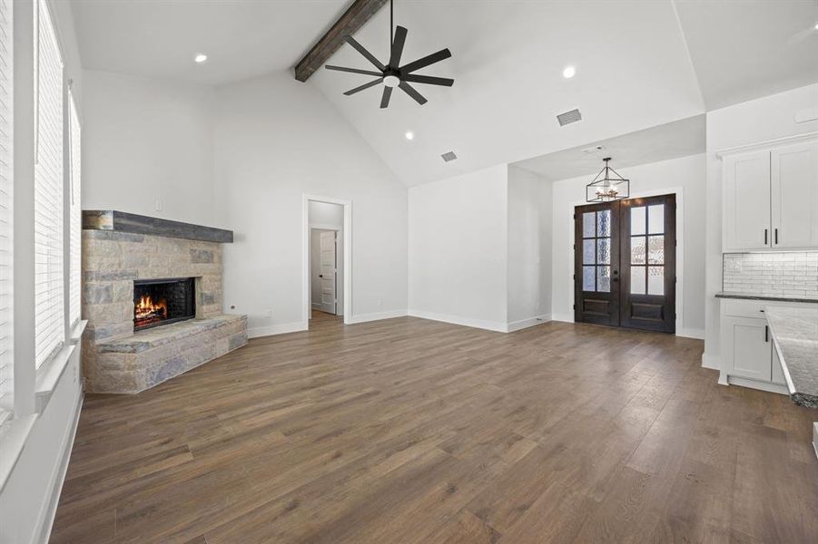 Unfurnished living room featuring a stone fireplace, dark wood-style floors, a chandelier, and ceiling fan
