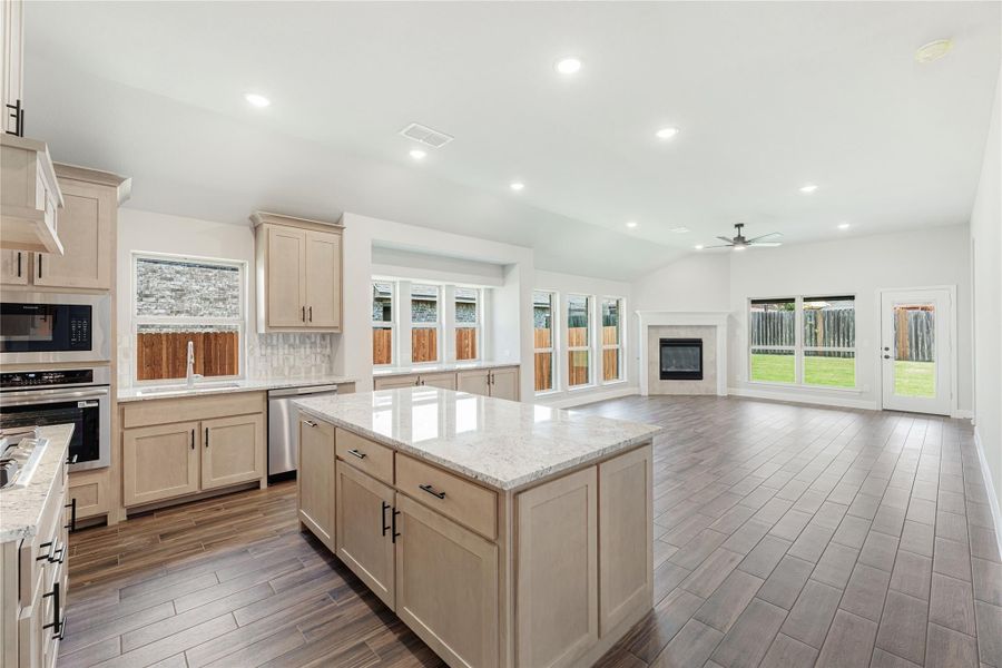 Open kitchen with center island, granite countertops, and light wood cabinets flowing into living area with fireplace Open kitchen with center island, granite countertops, and light wood cabinets flowing into living area with fireplace
