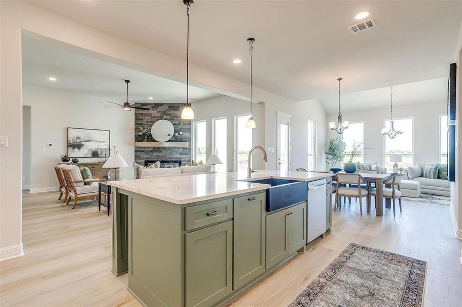 Kitchen featuring a stone fireplace, a kitchen island with sink, light wood-type flooring, and a wealth of natural light