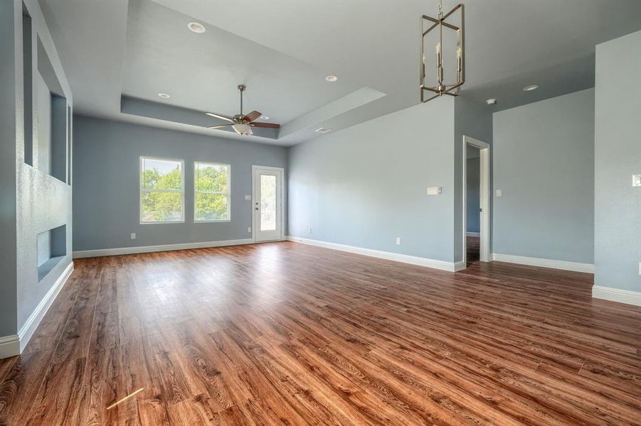 Unfurnished living room featuring ceiling fan with notable chandelier, hardwood / wood-style flooring, and a tray ceiling