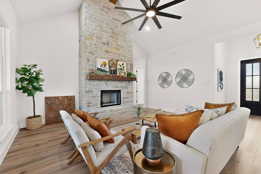 Living room with lofted ceiling, light wood finished floors, a stone fireplace, and ceiling fan