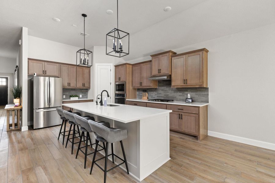 Dual tone kitchen with a kitchen breakfast bar, stainless steel appliances, a kitchen island with sink, light wood-style floors, and a chandelier