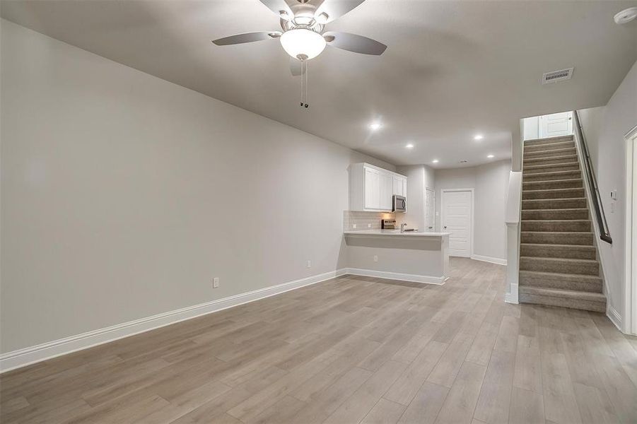 Unfurnished living room featuring recessed lighting, light wood finished floors, a ceiling fan, and stairs Unfurnished living room featuring recessed lighting, light wood finished floors, a ceiling fan, and stairs