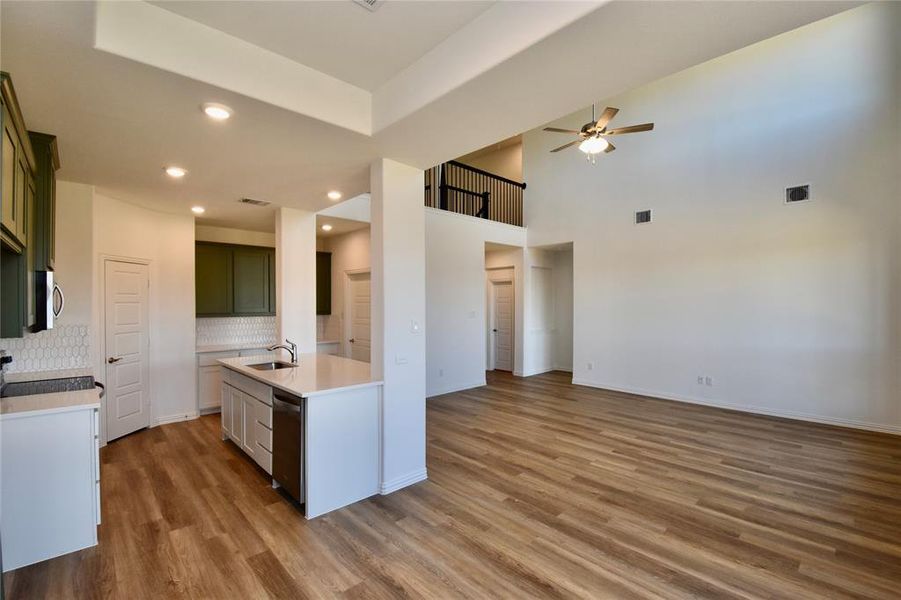Kitchen with open floor plan, light wood-type flooring, decorative backsplash, light stone countertops, and a towering ceiling