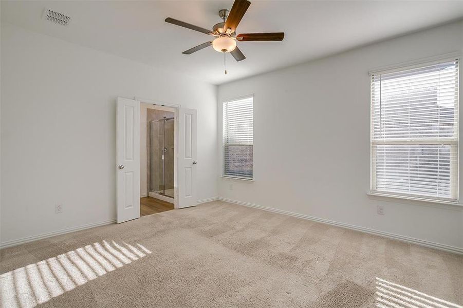 Unfurnished bedroom with ceiling fan, ensuite bath, light carpet, and multiple windows