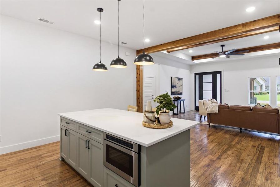 Kitchen island featuring a light-toned countertop, integrated microwave, and pendant lighting