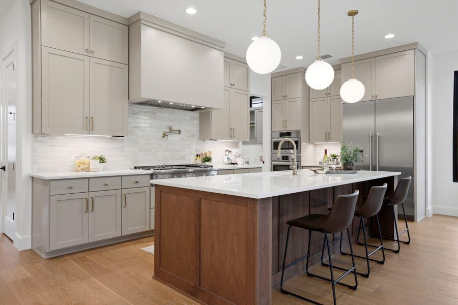 Two tone kitchen with dual tone cabinets, pendant lighting, stainless steel appliances, light wood-style floors, and a breakfast bar area