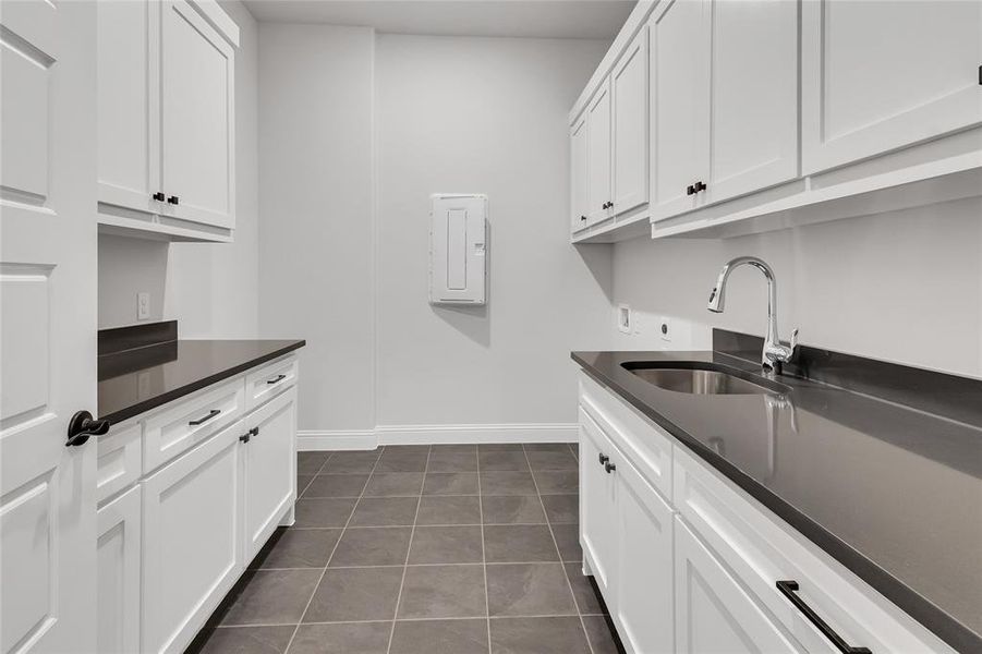 Laundry room with dark tile patterned flooring, cabinets, electric panel, sink, and hookup for a washing machine