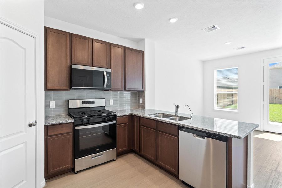 This spacious kitchen boasts soaring ceilings, Woodmont Cody cabinets in a Ginger stain, Granite Tulum countertops, stainless steel Whirlpool appliances, a modern Daltile backsplash, recessed lighting, and a pantry—all overlooking the expansive Great Room. This spacious kitchen boasts soaring ceilings, Woodmont Cody cabinets in a Ginger stain, Granite Tulum countertops, stainless steel Whirlpool appliances, a modern Daltile backsplash, recessed lighting, and a pantry—all overlooking the expansive Great Room.