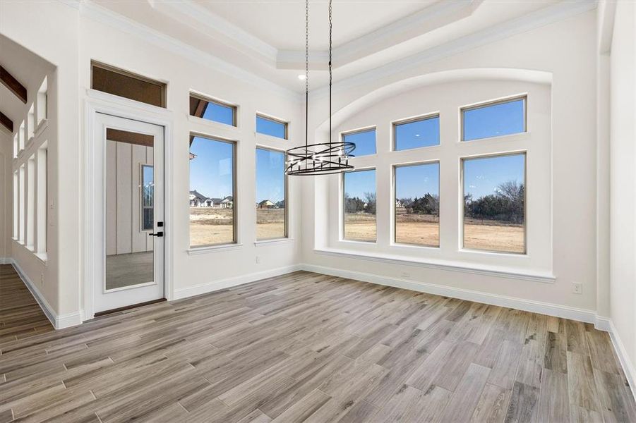 Breakfast room area with custom flooring floors, ornamental molding, a raised ceiling, and an inviting decorative lighting