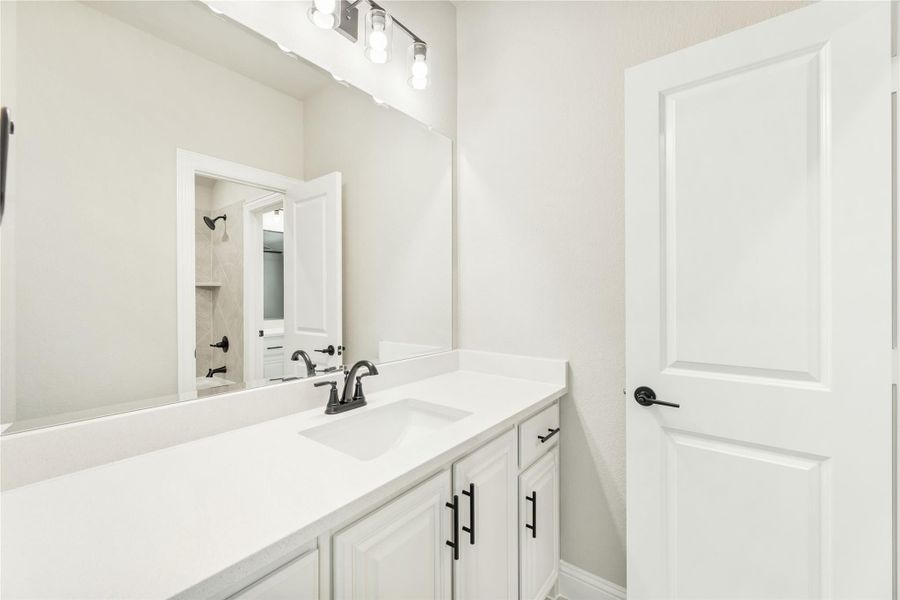 Bathroom vanity with white cabinets, quartz countertop, single sink, black fixtures, and large mirror with overhead lighting. Bathroom vanity with white cabinets, quartz countertop, single sink, black fixtures, and large mirror with overhead lighting.