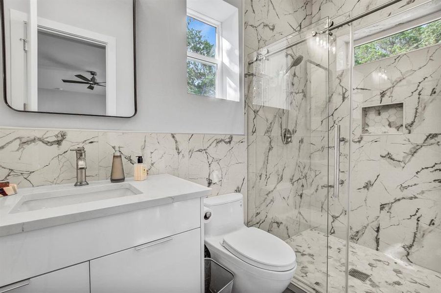 Full bathroom in the moth in law suite featuring vanity, a marble finish shower, and tile walls