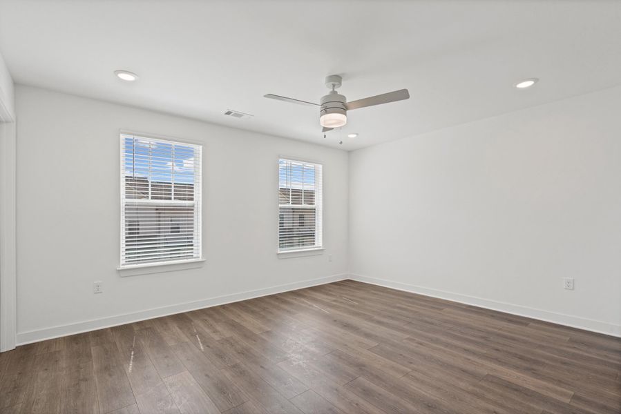 Expansive room featuring wood-finish flooring, two windows with blinds, a ceiling fan, and recessed lighting